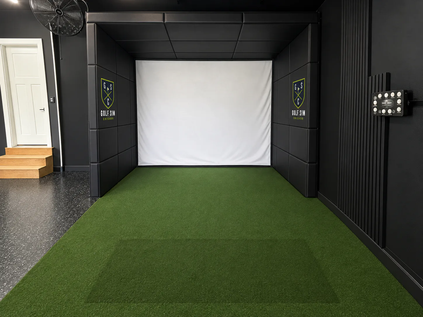 Completed Naperville garage golf simulator with a black padded enclosure, white impact screen, turf, and branded wall panels