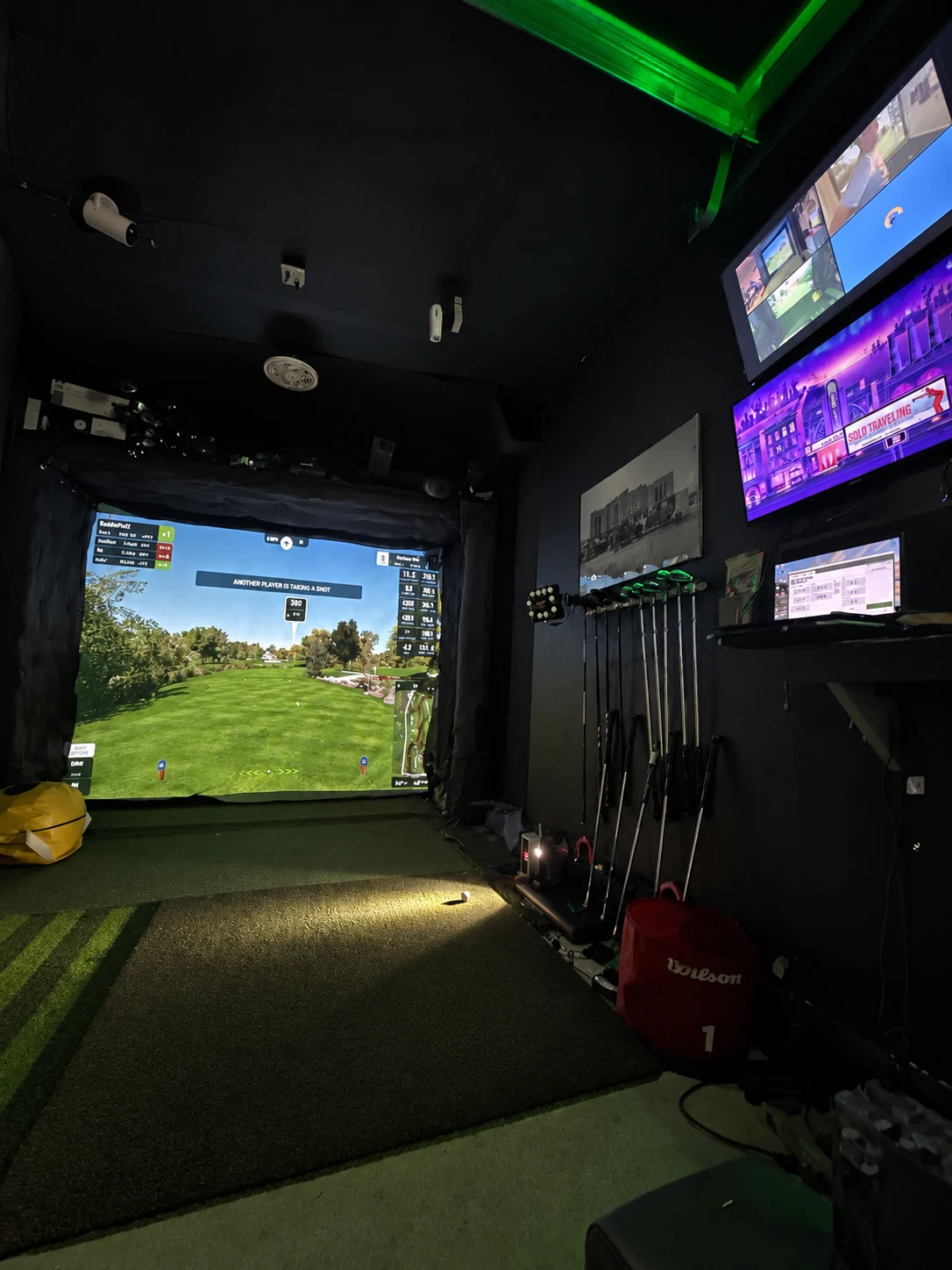 Completed Yorkville garage golf simulator with a curtained screen, turf hitting area, club rack, wall-mounted displays, and green accent lighting